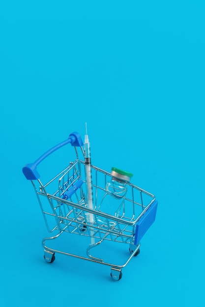 Chariot de supermarché avec seringues et ampoule sur fond bleu