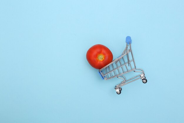 Chariot de supermarché à la tomate sur fond bleu.