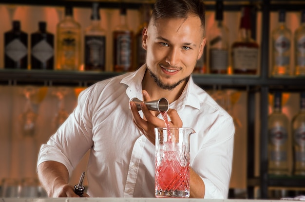 Le charmant barman verse l'alcool du jigger dans un verre à mélange rempli de glace