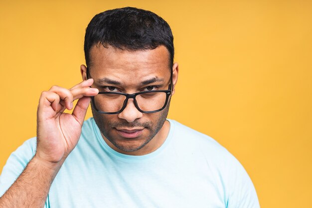 Charmant beau. Confiant jeune homme indien ajustant ses lunettes en se tenant isolé sur fond jaune.