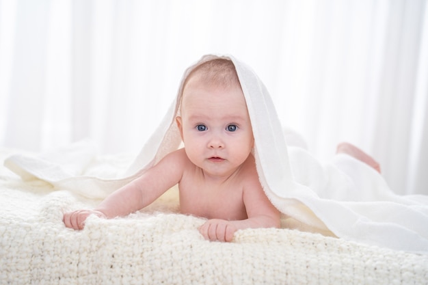 Charmant bébé doux est allongé sur le lit sous une couverture blanche