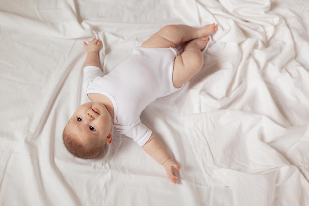 Charmant bébé nouveau-né dans un body blanc allongé sur le dos sur un tissu blanc. vue de dessus. produits pour enfants. concept d'enfance et de maternité heureuses. espace pour le texte. Photo de haute qualité