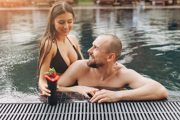 Charmant couple se détendant dans la piscine et dégustant des cocktails en été