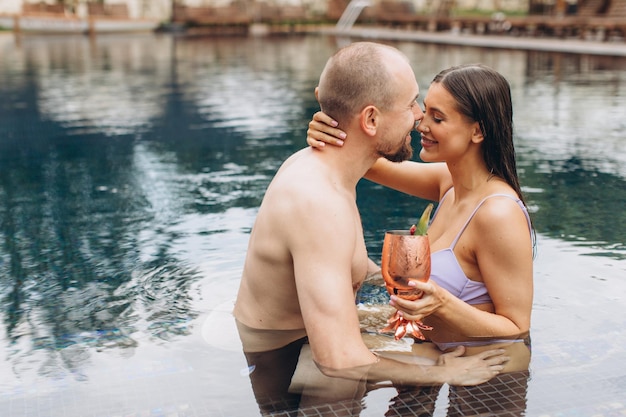 Charmant couple se détendant dans la piscine et dégustant des cocktails en été