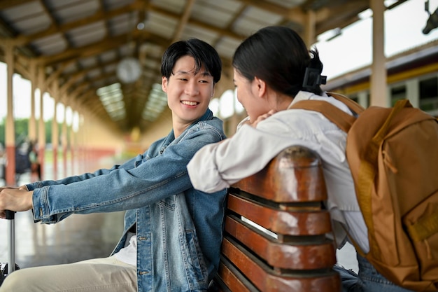Un charmant couple de touristes asiatiques aime parler sur un banc sur le quai avant de monter dans le train