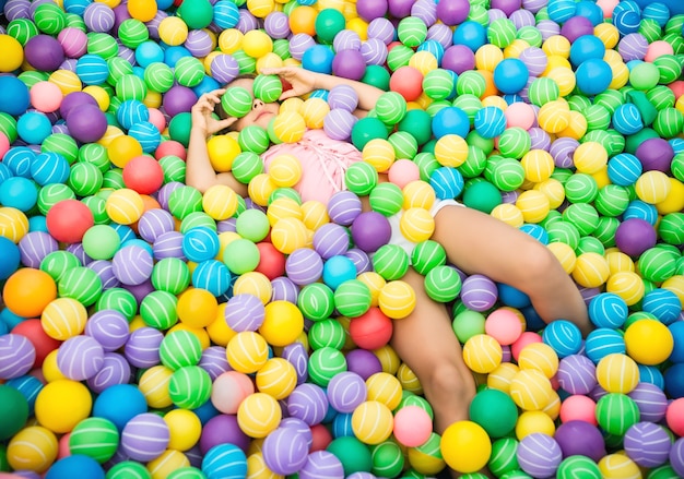 Charmant enfant couché dans la piscine avec des boules en plastique multicolores. Fille habillée en chemisier rose et short blanc