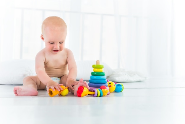 Charmant enfant gai dans une couche rit et joue assis dans sa chambre confortable