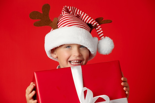 Charmant garçon souriant dans la casquette de Noël du Père Noël avec un cadeau