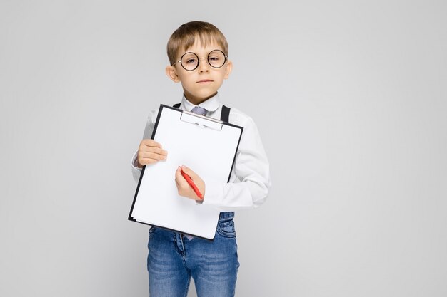 Un charmant garçon vêtu d'une chemise blanche, de jarretelles, d'une cravate et d'un jean léger Le garçon tient un stylo et des feuilles pour les notes