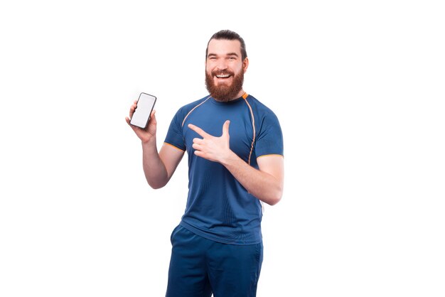 Charmant jeune homme barbu fitness pointant sur smartphone sur blanc