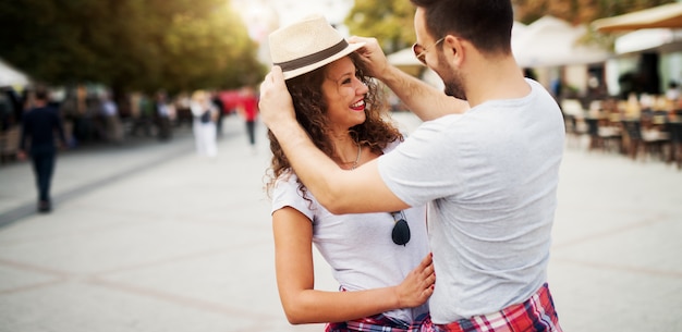 Charmant jeune homme mettant un chapeau sur une petite amie dans la promenade romantique.