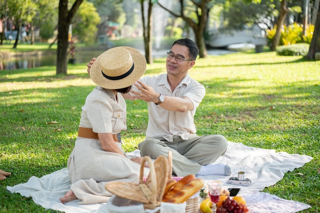 Un charmant mari asiatique porte un chapeau à sa femme alors qu'ils pique-niquent ensemble dans le parc.