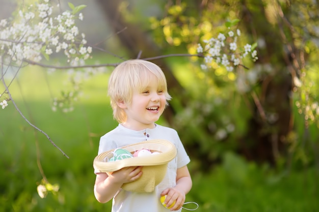 Charmant petit garçon à la recherche d'oeufs de Pâques dans le parc du printemps le jour de Pâques