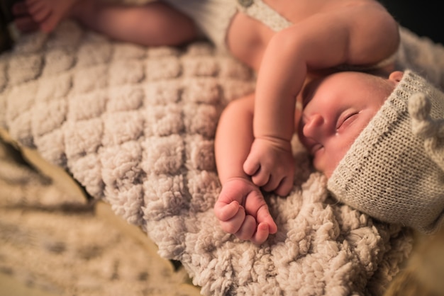 Charmant petit nouveau-né vêtu d'un costume tricoté et d'un bonnet, il dort sur un plaid en laine douce. Le concept d'adorables petits enfants