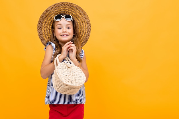 Charmante belle fille glamour dans un chapeau de paille et des lunettes sur un mur jaune