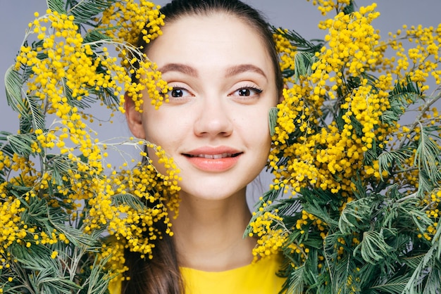 Charmante belle fille sourit et regarde la caméra tient un mimosa jaune parfumé