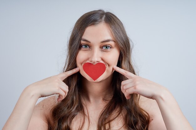 Charmante blonde avec un cœur en papier sur ses lèvres. Joyeuse saint Valentin.