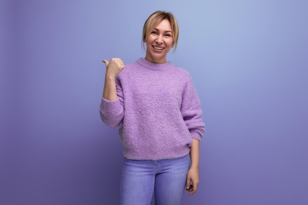 Une charmante blonde mignonne dans un pull lavande souriante sur un fond violet avec un espace de copie