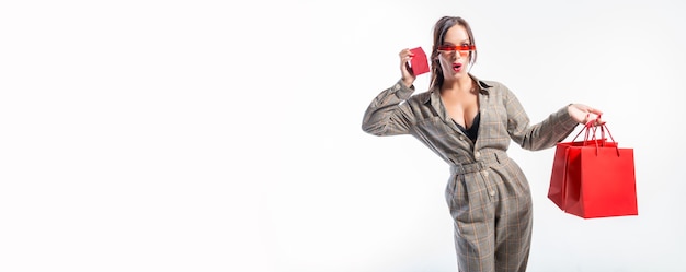 Charmante brune à lunettes posant dans le studio avec des sacs rouges et une boîte à bijoux