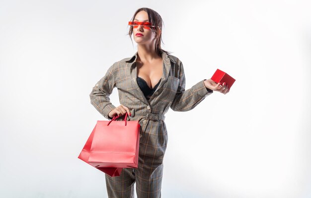 Charmante brune à lunettes posant dans le studio avec des sacs rouges et une boîte à bijoux