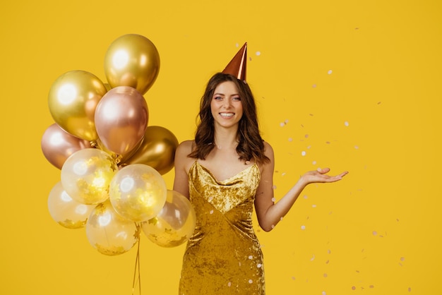 Charmante dame heureuse tenant des ballons ayant une fête d'anniversaire sur fond de studio jaune avec