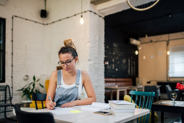 Charmante étudiante prenant des notes au café.