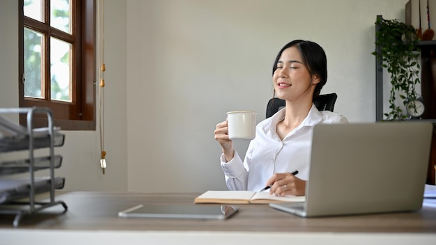 Une charmante femme d'affaires asiatique apprécie son café du matin à son bureau dans son bureau