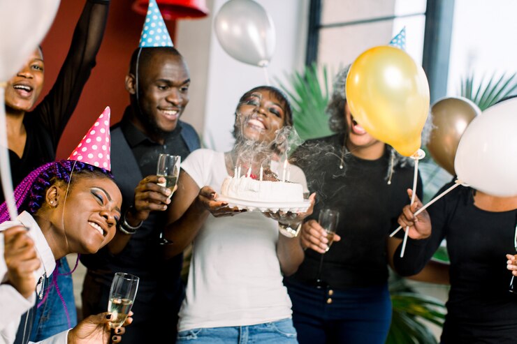 Photo charmante femme africaine soufflant sur des bougies sur le gâteau d'anniversaire après avoir fait son souhait à la fête