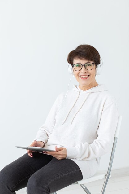 Charmante femme d'âge moyen mince dans des lunettes et un pull est assise sur une chaise et écoute son préféré