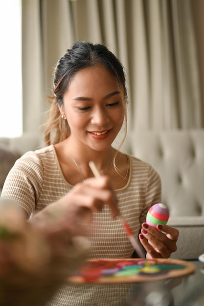 Charmante femme asiatique peignant un oeuf de Pâques avec une aquarelle préparant un truc de Pâques à la maison