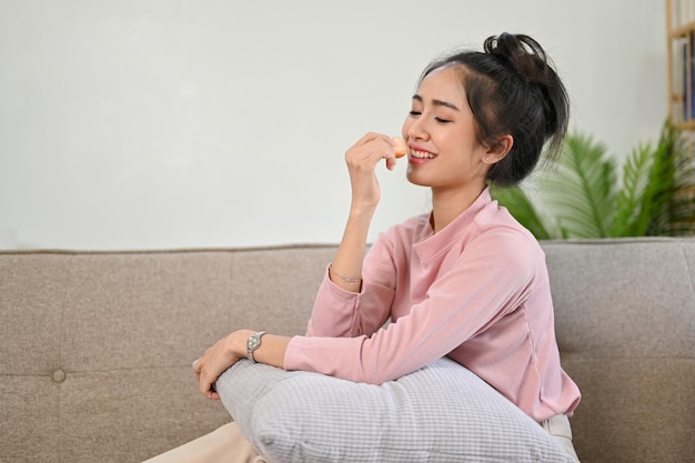 Charmante femme asiatique se relaxant sur son canapé en mangeant des beignets dans son salon