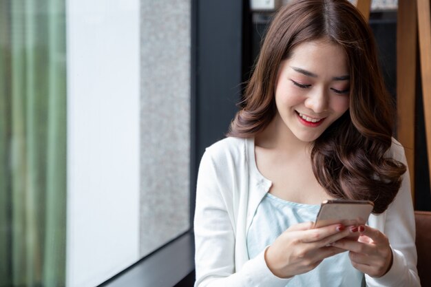 Charmante femme asiatique sourire lecture de bonnes nouvelles sur téléphone mobile pendant le repos dans un café