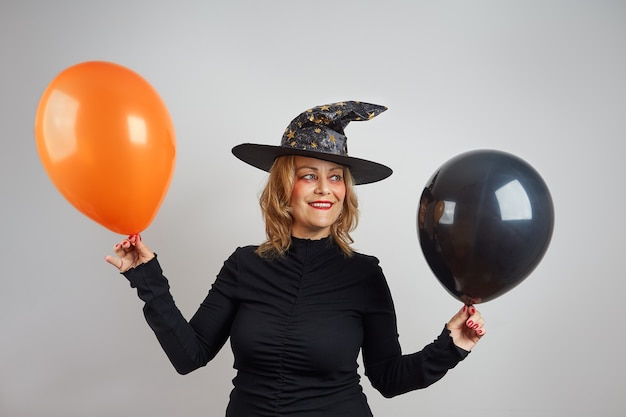 Charmante femme blonde en costume d'halloween avec des ballons noir-orange sur fond gris.