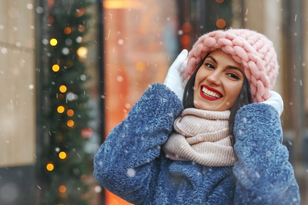 Charmante femme brune en manteau marchant dans la ville par temps de neige. Espace libre