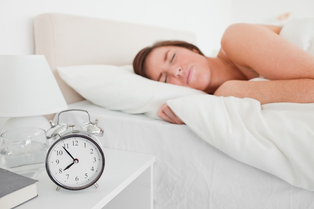 Charmante femme brune se réveiller avec une horloge en position couchée