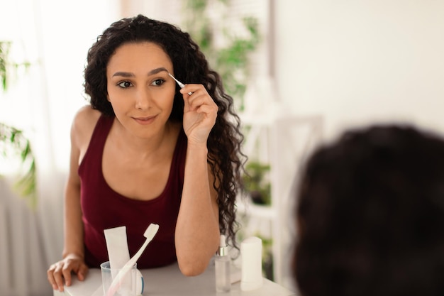 Charmante femme du millénaire épilant les sourcils près du miroir à la maison copie espace routines de beauté du matin