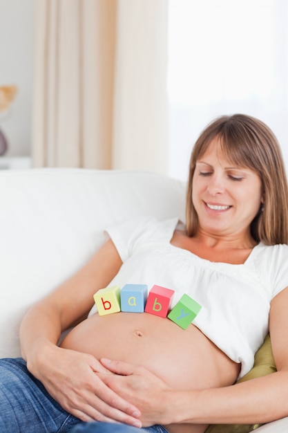 Charmante femme enceinte jouant avec des blocs de bois en position couchée sur un canapé