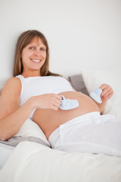 Charmante femme enceinte jouant avec des petites chaussettes en position couchée sur un lit