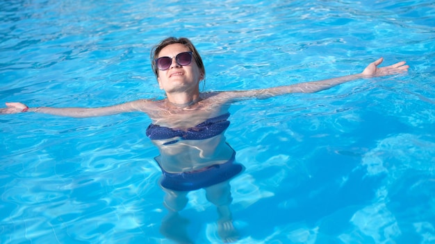 Charmante femme à lunettes de soleil aime nager dans l'eau turquoise de la piscine