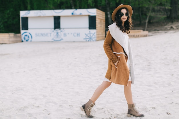 Charmante femme en manteau marchant sur la plage