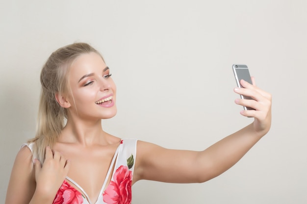 Charmante femme mignonne faisant autoportrait sur smartphone sur fond gris