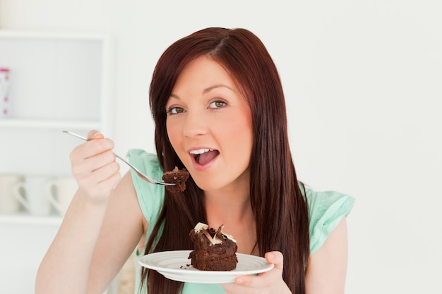 Charmante femme rousse manger un gâteau dans la cuisine