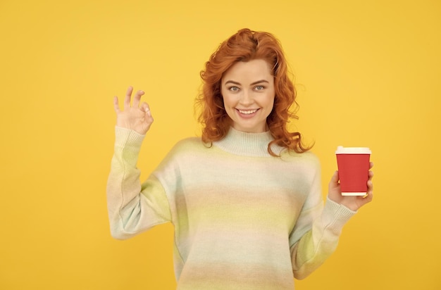 Charmante femme rousse visage portrait boire du café à partir d'une tasse de papier montrer ok geste parfait