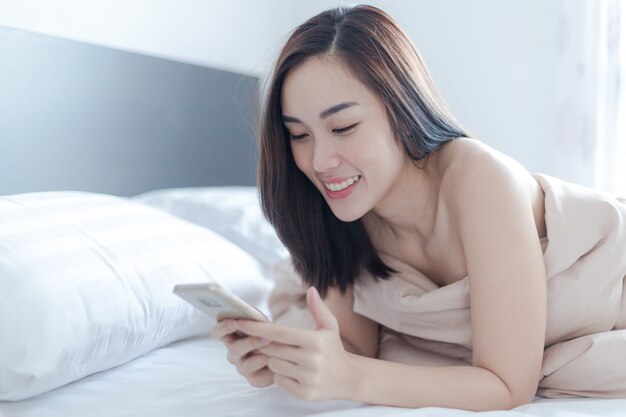 Charmante femme sexy joue sur téléphone portable sur le lit