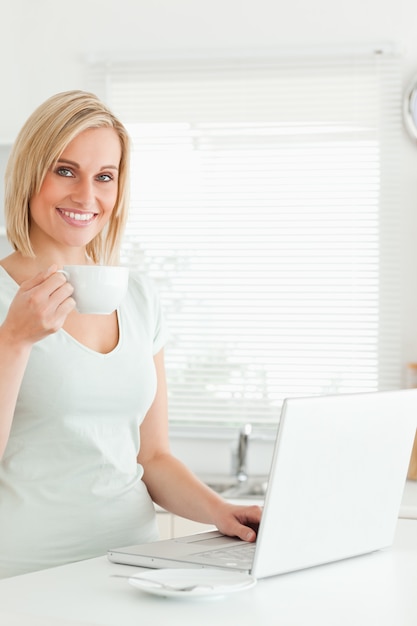 Charmante femme avec une tasse de café et un ordinateur portable regardant dans la caméra