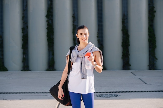 Charmante femme en tenue sportive debout dans la rue tenant de l'eau