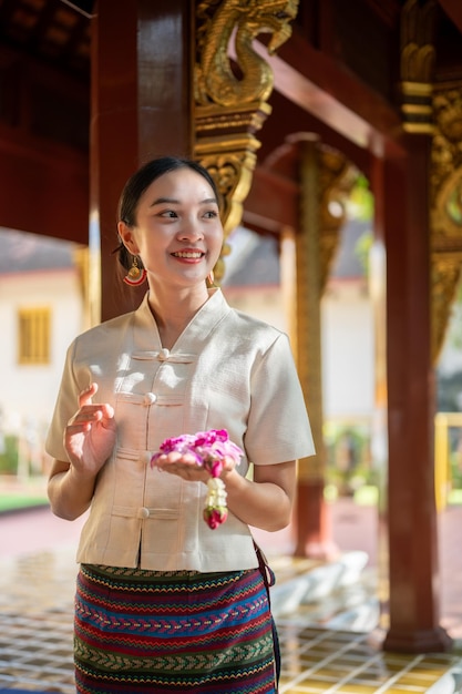 Une charmante femme thaïlandaise en robe traditionnelle thaïlandaise est dans un temple faisant un mérite