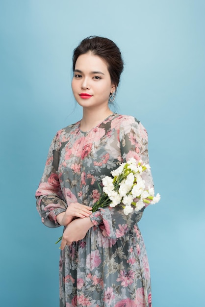 Charmante fille asiatique en robe à fleurs debout sur fond bleu