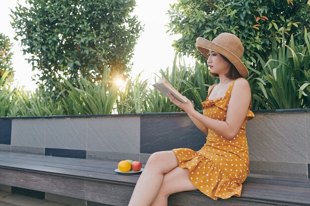 Charmante fille asiatique se relaxant dans le parc printanier tout en lisant un livre.