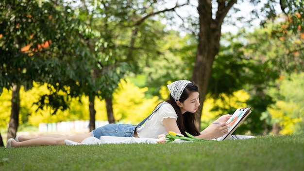 Charmante fille femme assise sur un plaid au parc en journée d'été ensoleillée et à l'aide d'aquarelle